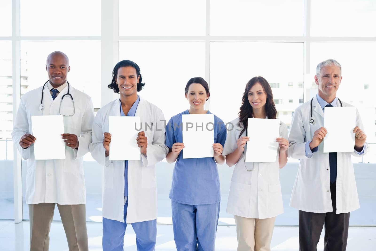 Medical team standing upright holding blank sheets in front of the bright window