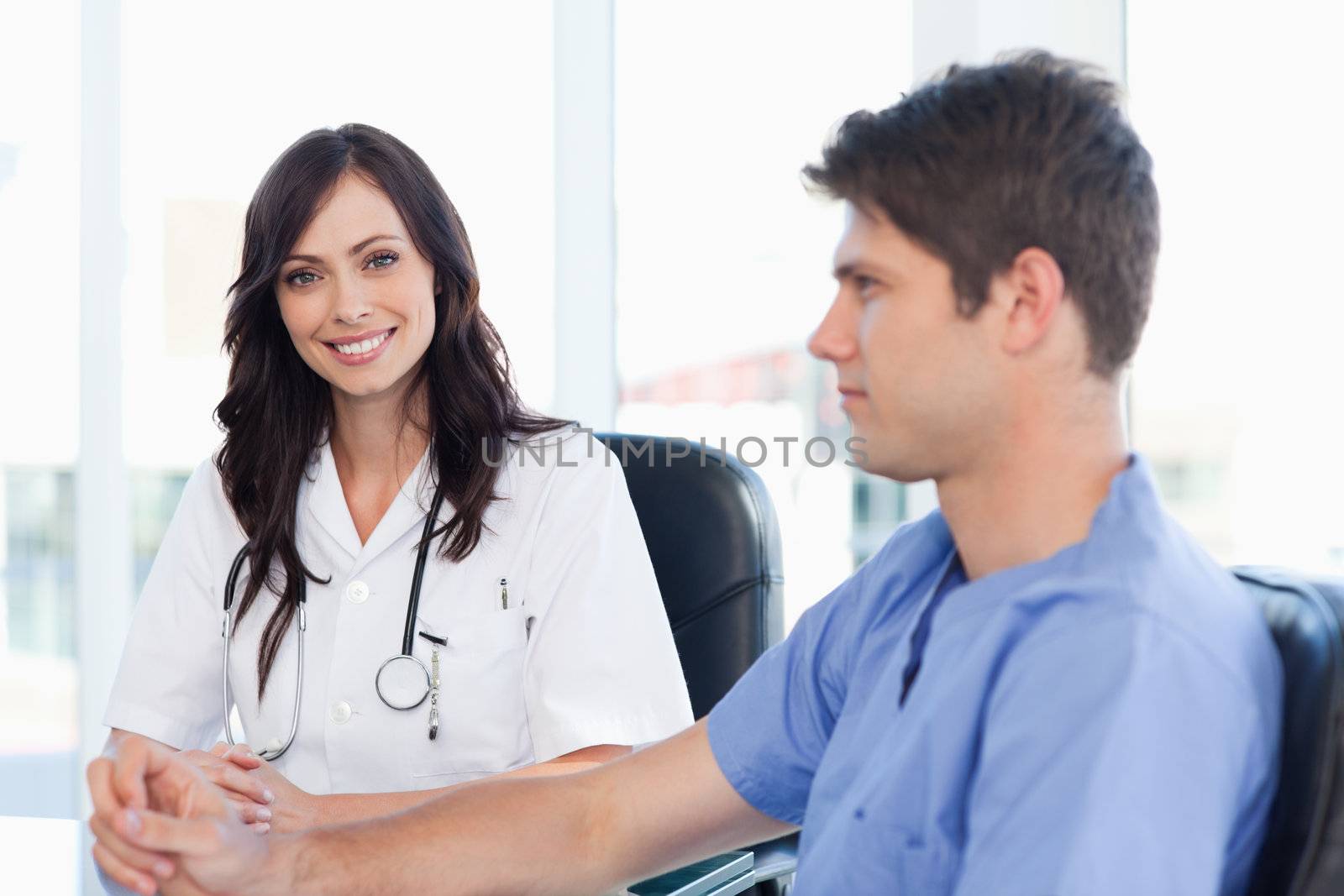 Young nurse sitting at the desk looking at her co-worker by Wavebreakmedia