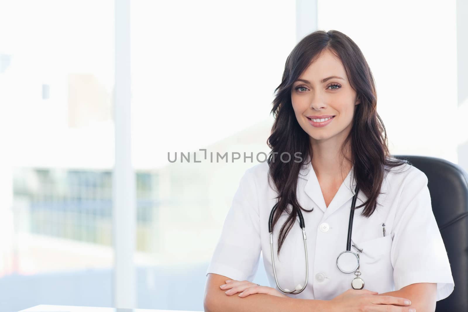 Young doctor sitting on a black chair at the desk with her arms  by Wavebreakmedia