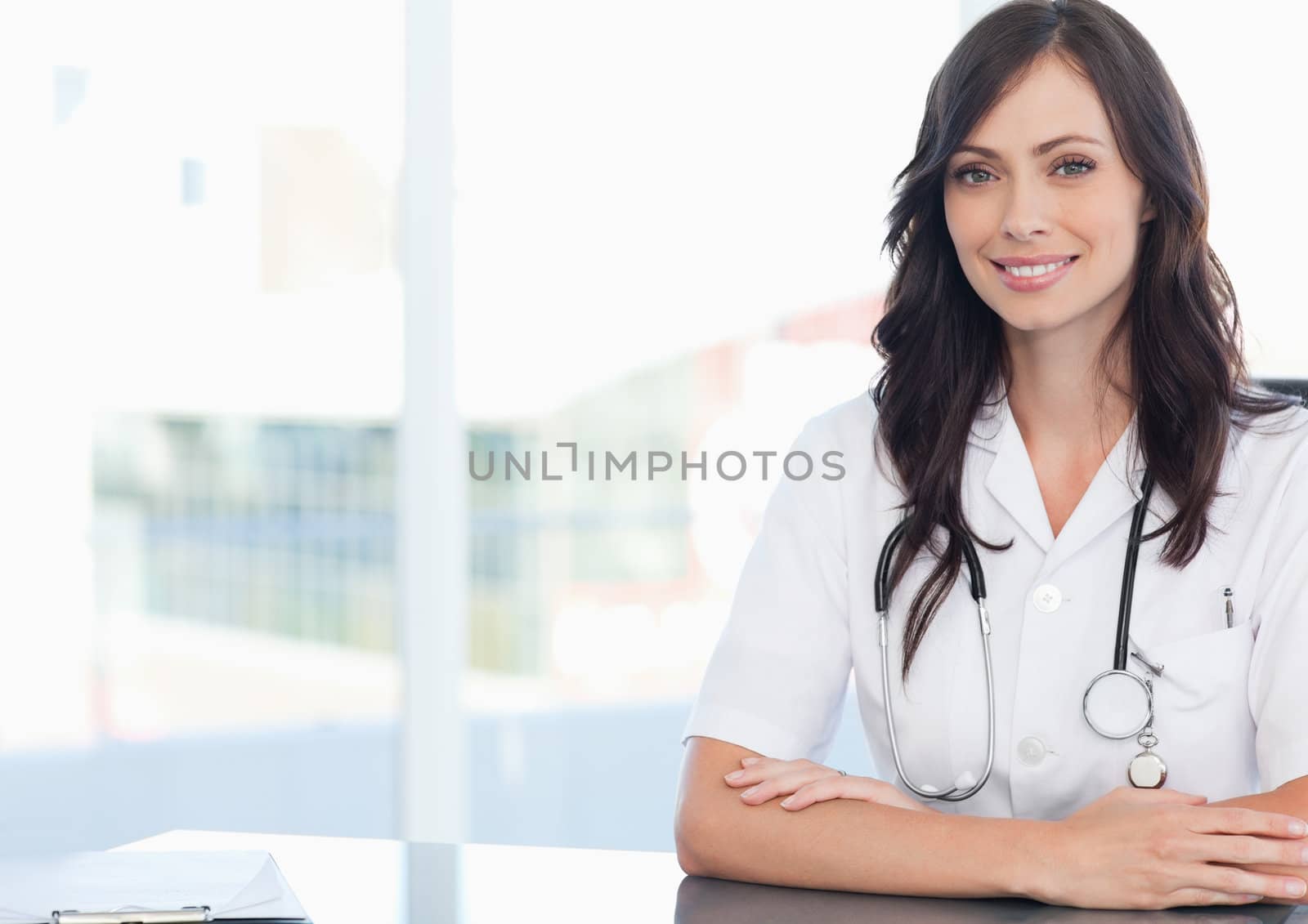 Young smiling doctor sitting at the desk near a clipboard by Wavebreakmedia