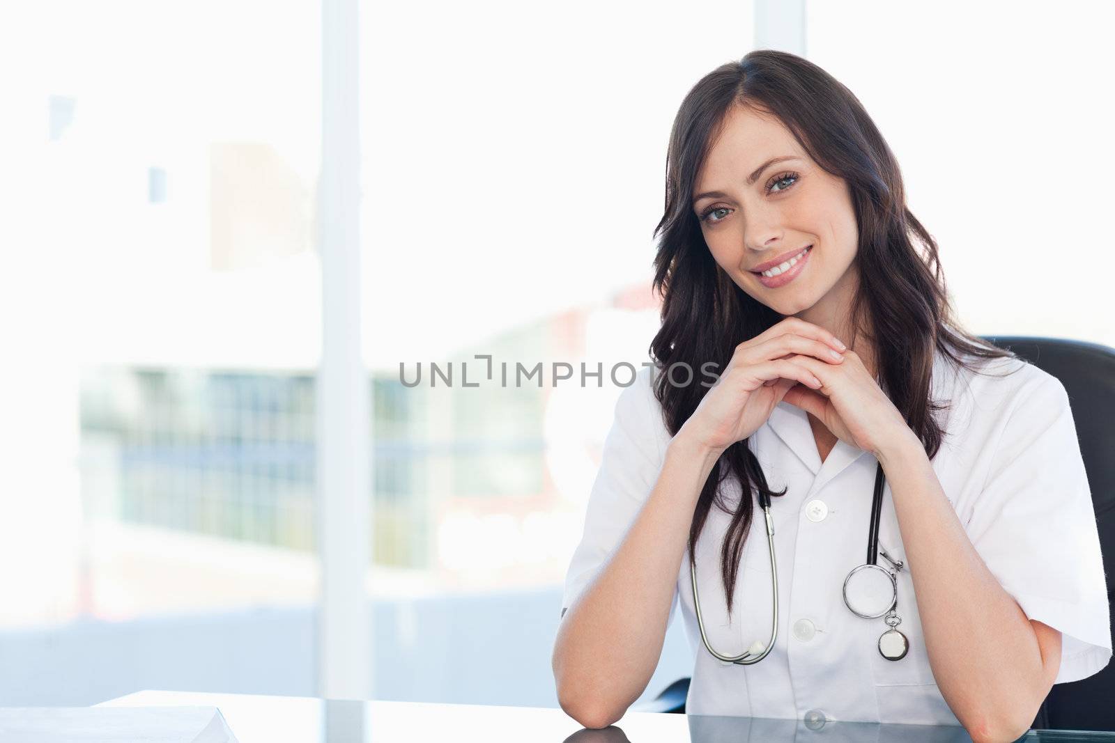 Young nurse sitting at the desk with her hands crossed and leani by Wavebreakmedia