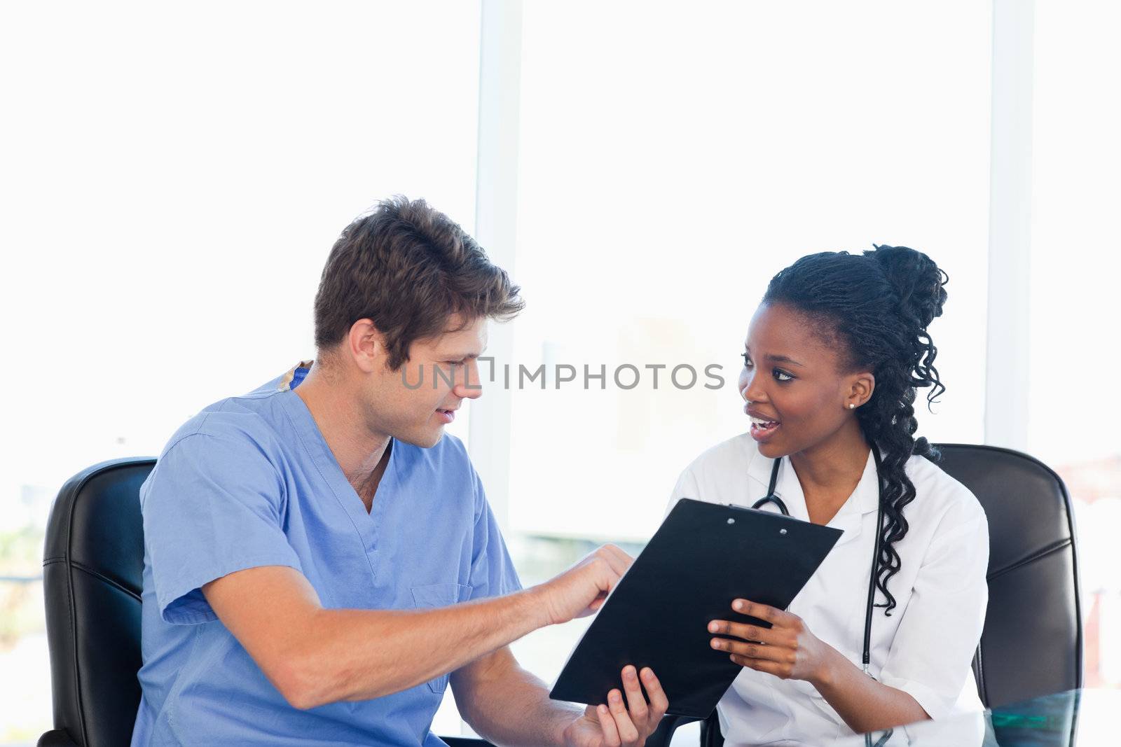 Young serious doctor showing something on a clipboard to his smiling co-worker