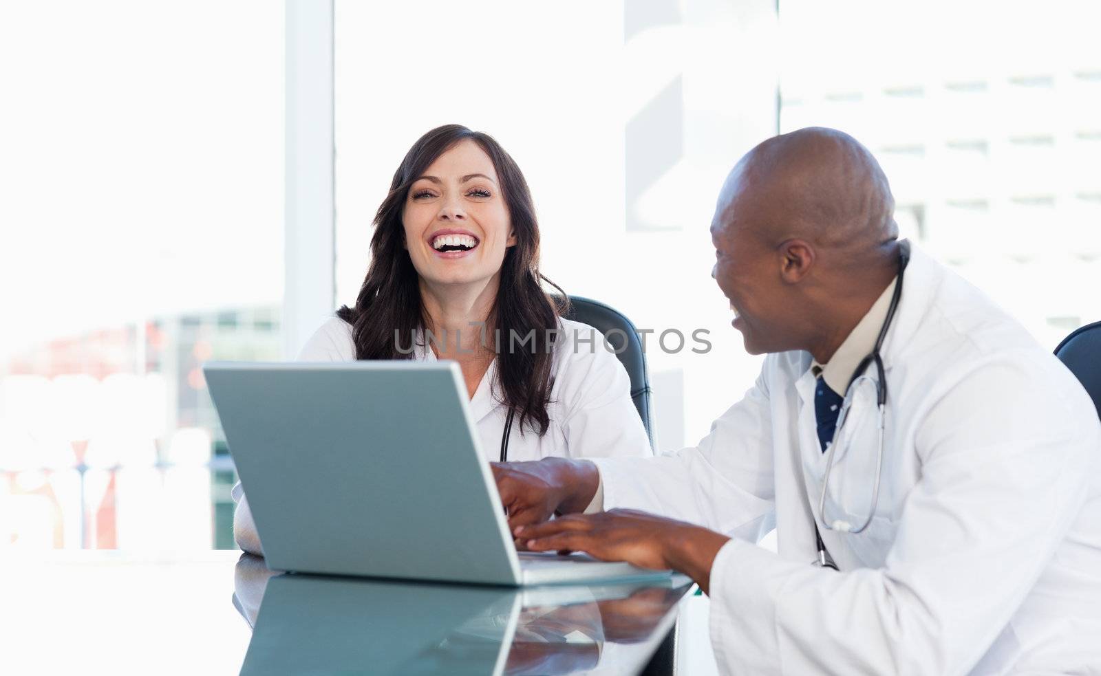 Young nurse laughing while working on a laptop with a relaxed co-worker