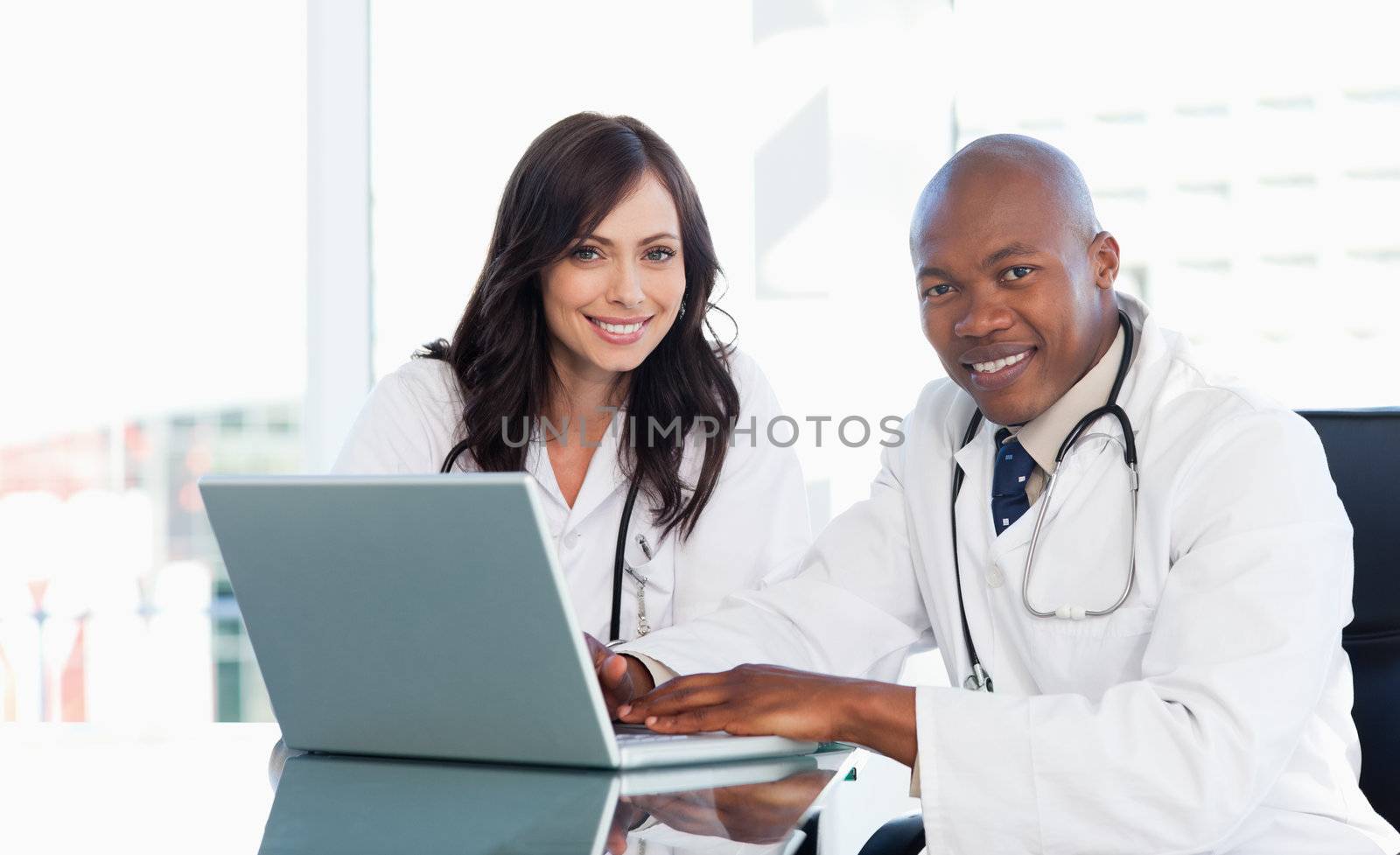 Smiling medical staff working in front of a laptop while sitting by Wavebreakmedia