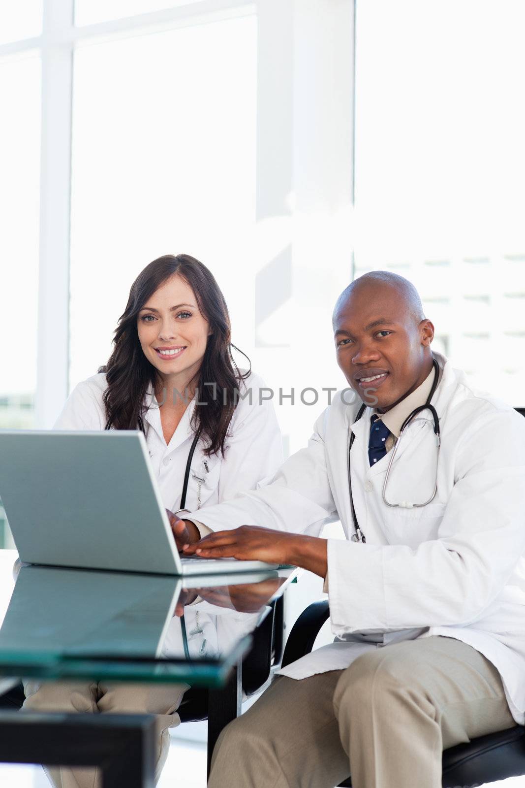 Smiling doctor working on a laptop while accompanied by his coll by Wavebreakmedia