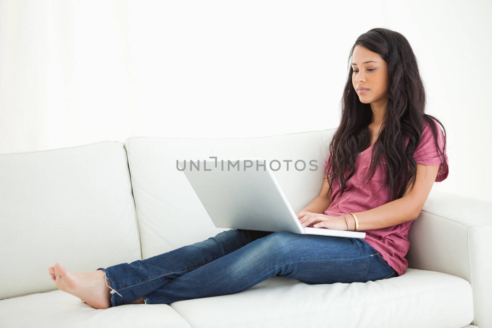 Unsmiling Latino student sitting on a sofa with her laptop