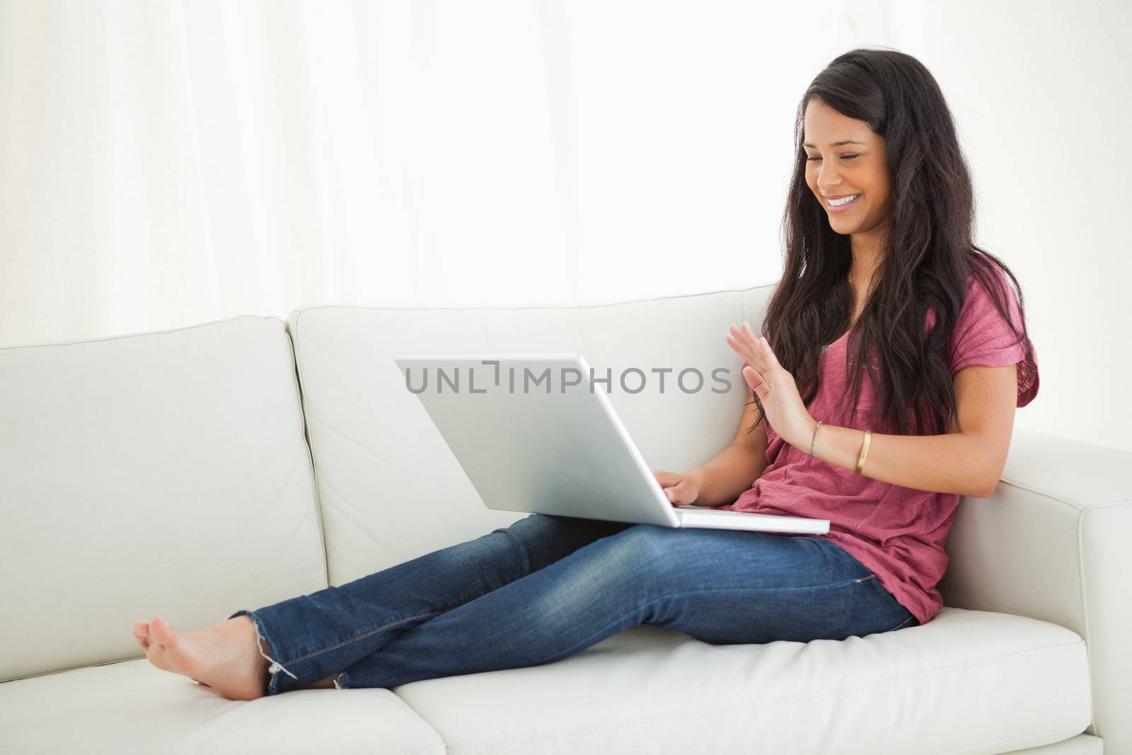 Latino student saying hello at the webcam while sitting on a sofa
