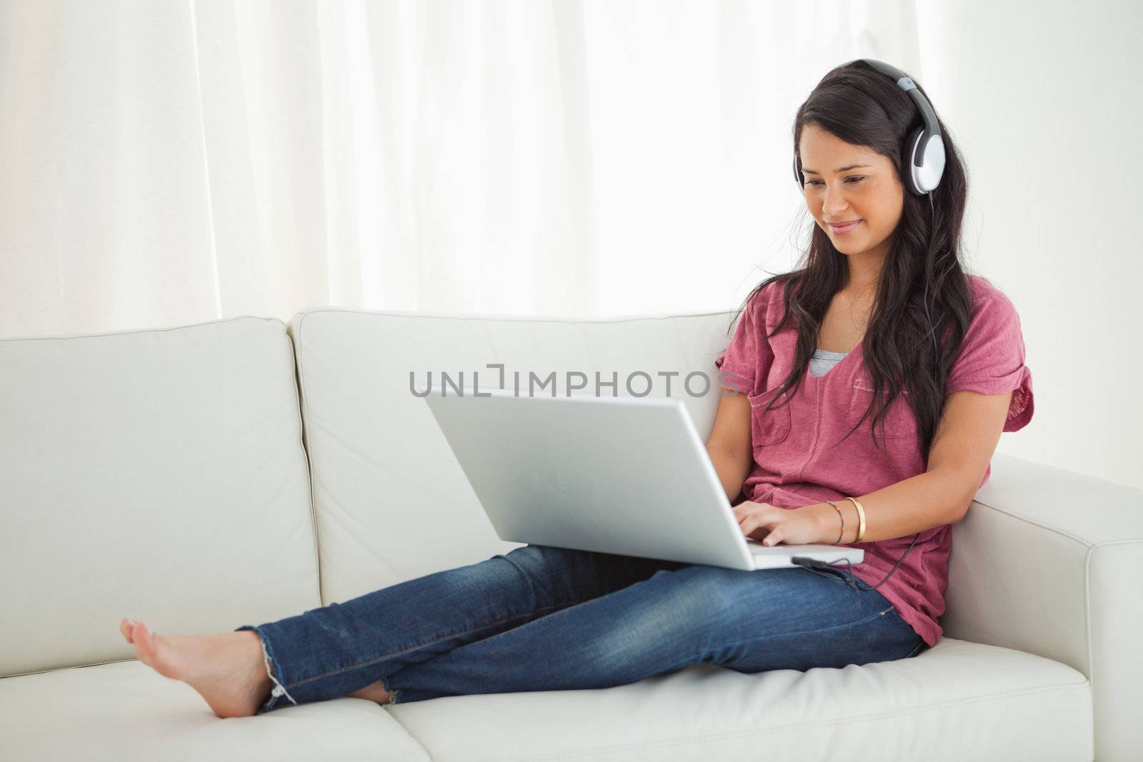 Latino student wears earphone using a laptop while sitting on a sofa