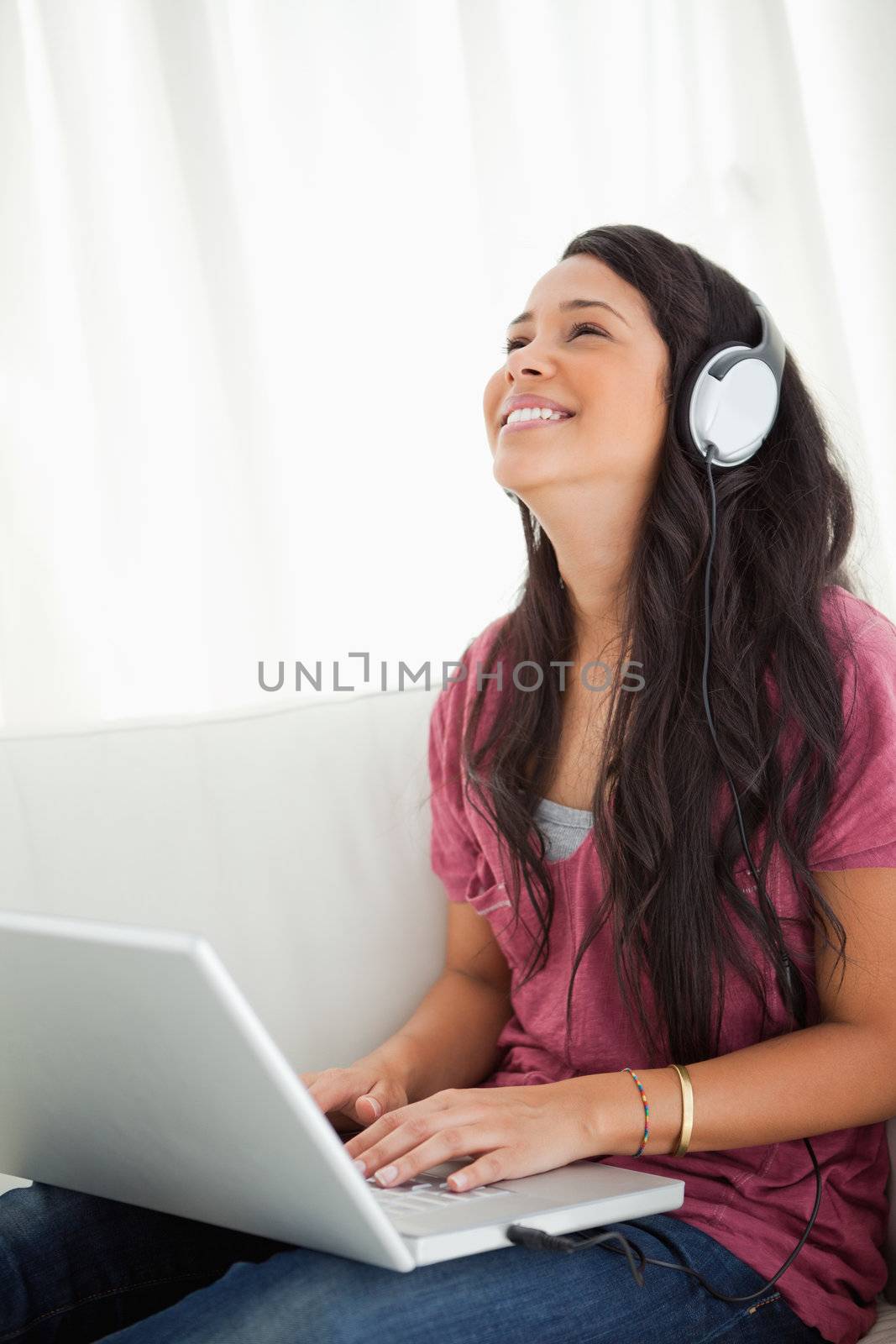 Close-up of a laughing Latino student using a laptop while enjoying music on her sofa