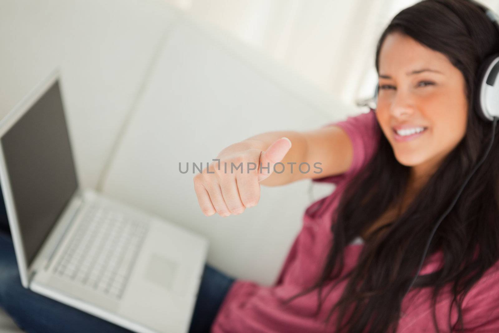 Thumb-up of a student with a laptop on the sofa