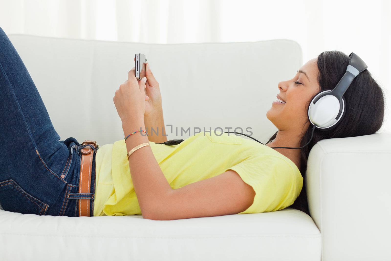Smiling young woman watching a video with her smartphone while lying on a sofa