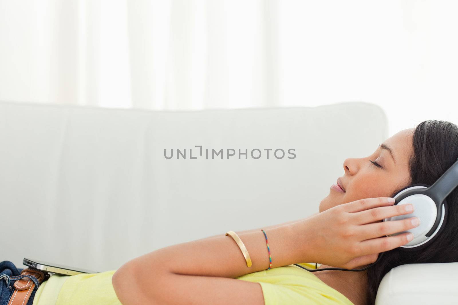 Young Latino listening music on a smartphone while lying on a sofa