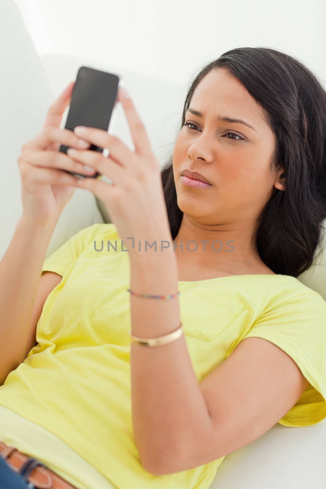 Close-up of a Latino frowning while looking her smartphone while lying on a sofa