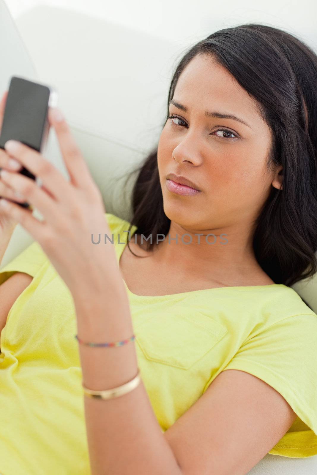 Portrait of a sad Latino holding her smartphone while lying on a sofa