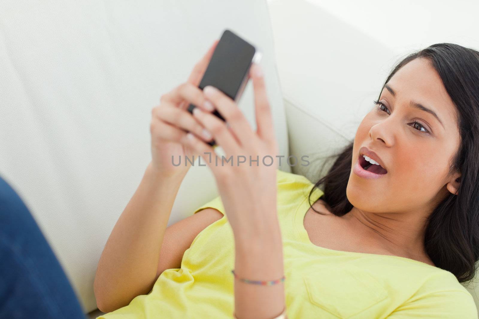 Close-up of a surprised Latino looking her smartphone while lying on a sofa