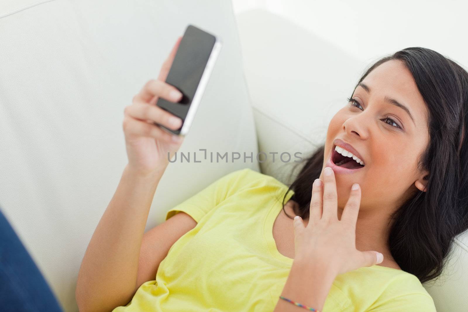 Close-up of a surprised Latino woman looking her smartphone while lying on a sofa