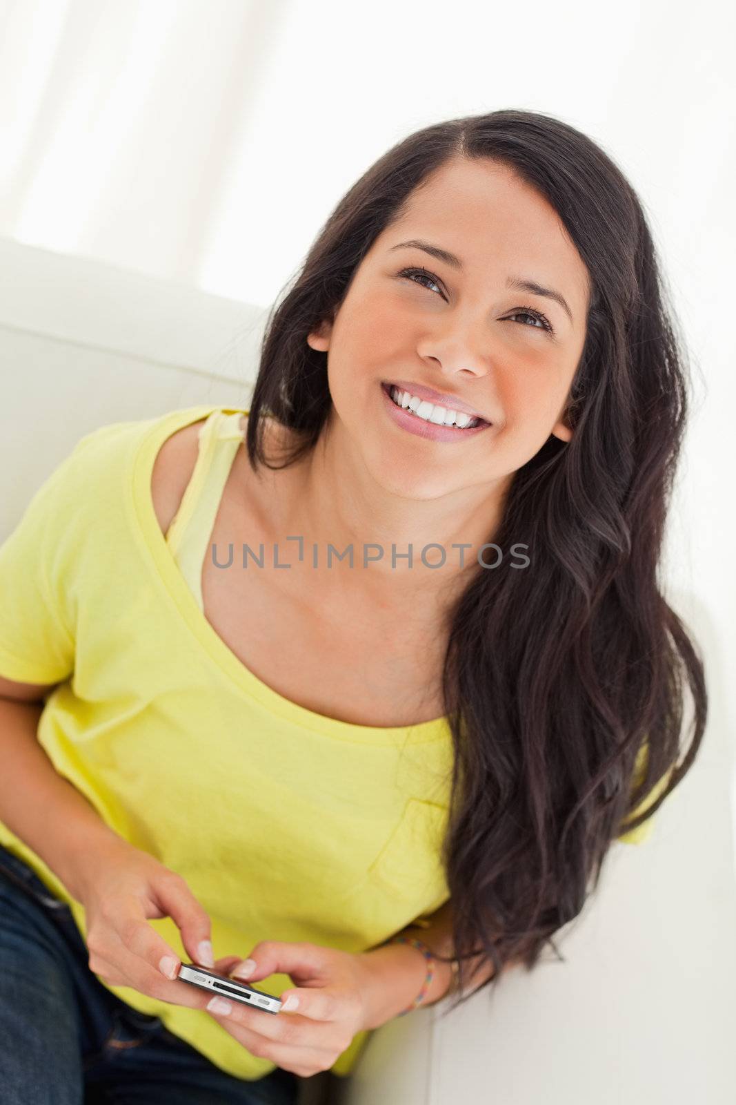 High-angle view of a happy Latino looking up while sitting on a sofa with her smartphone