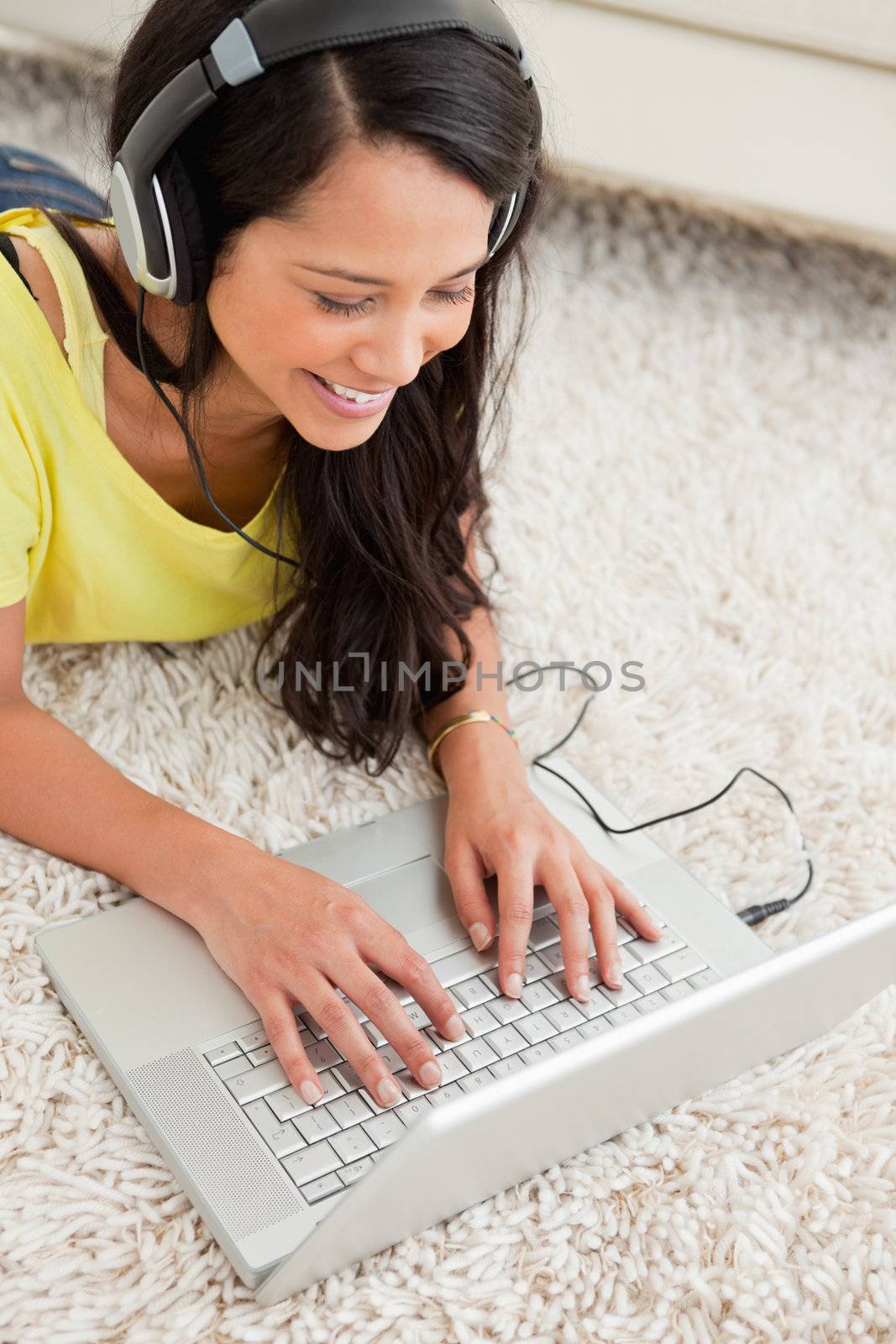 Close-up of a smiling Latin chatting on a laptop while lying on the floor with earphones