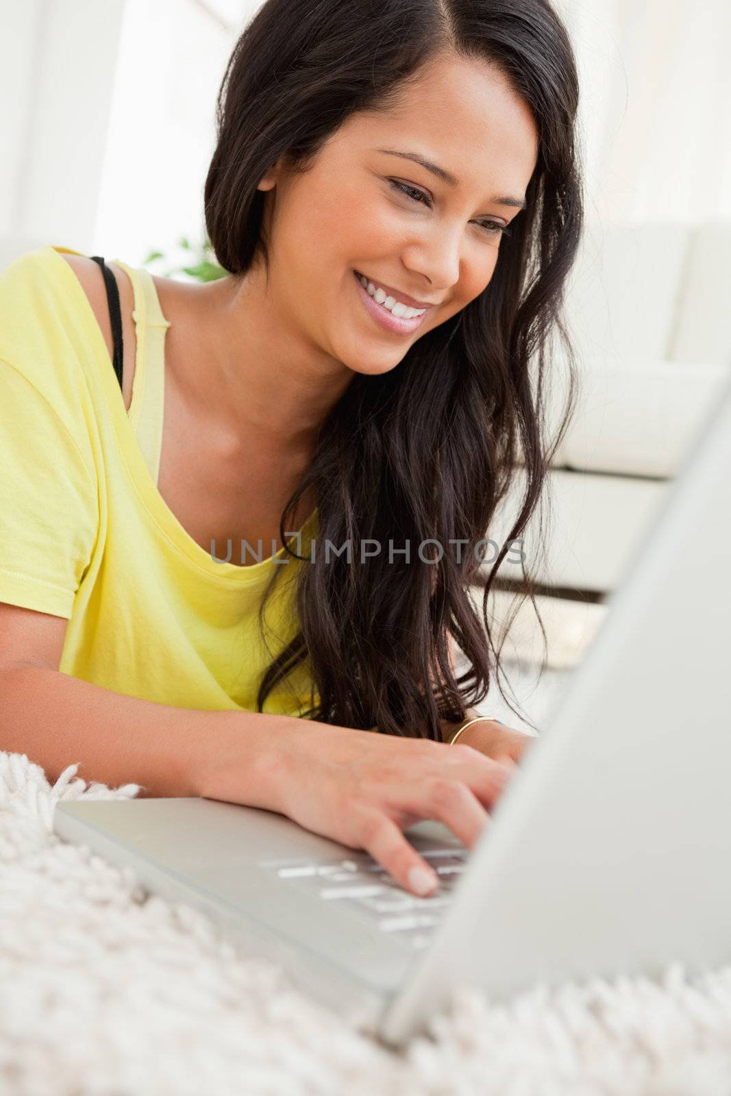 Close-up of a beaming Latin chatting on a laptop while lying on the floor