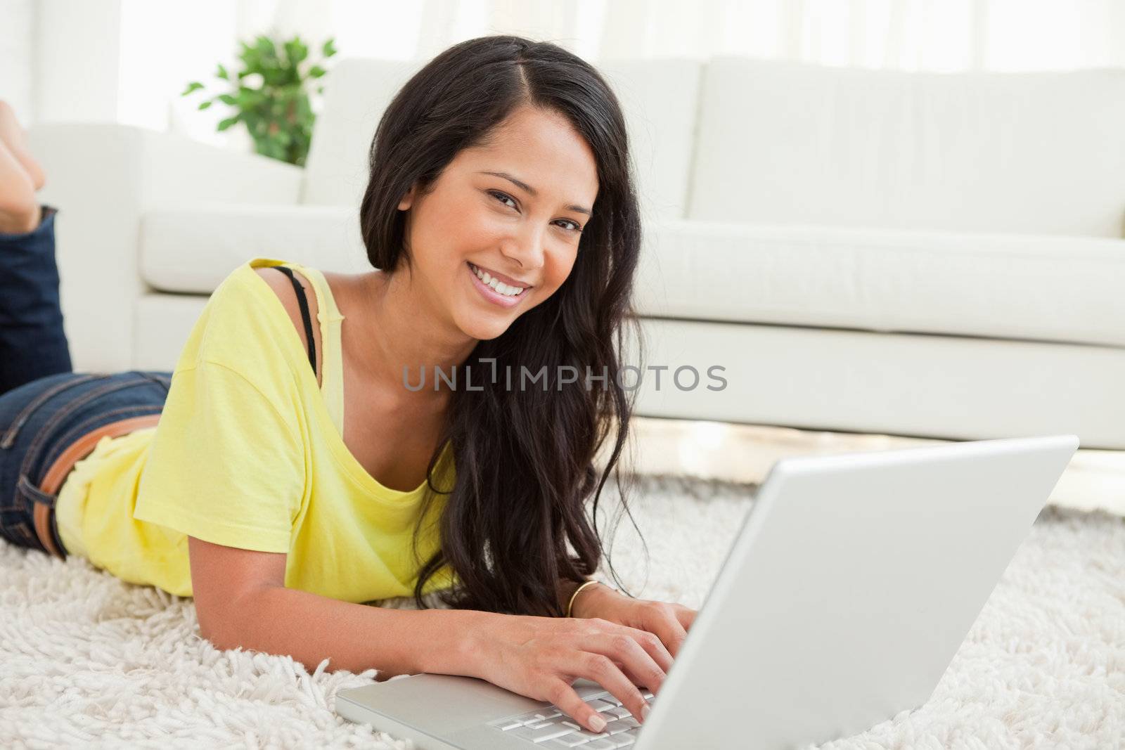 Portrait of a beaming Latin woman using a laptop while lying on the floor