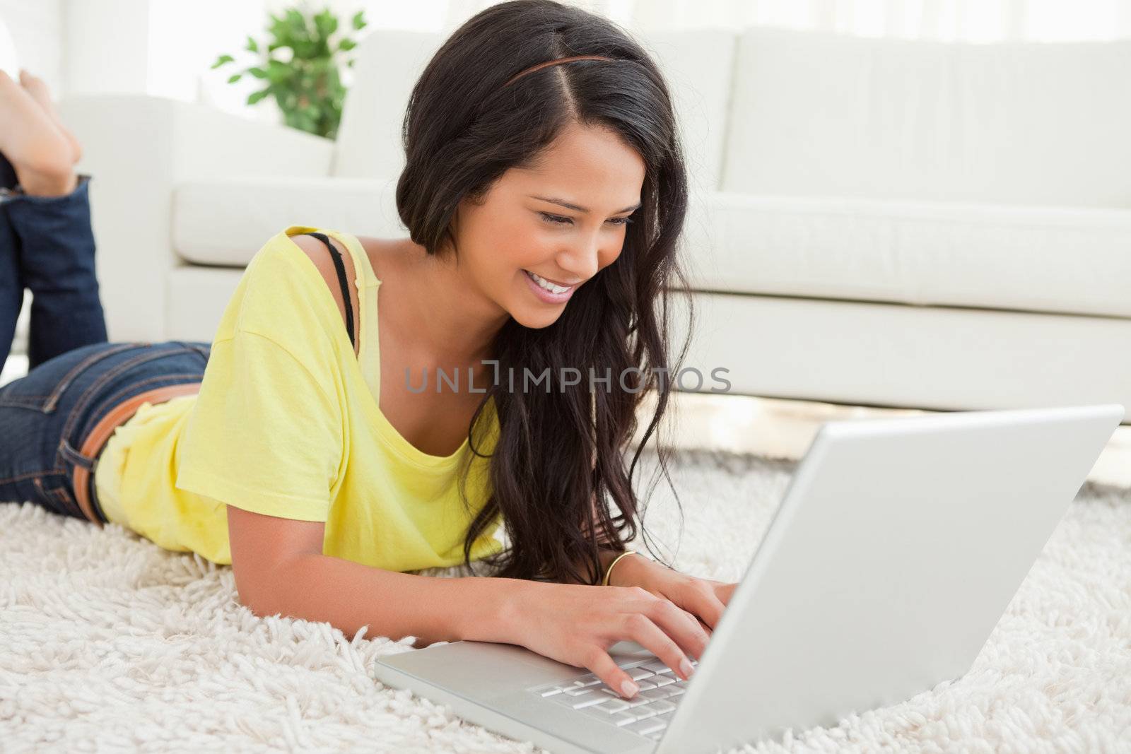 Beaming Latin woman using a laptop while lying on the floor