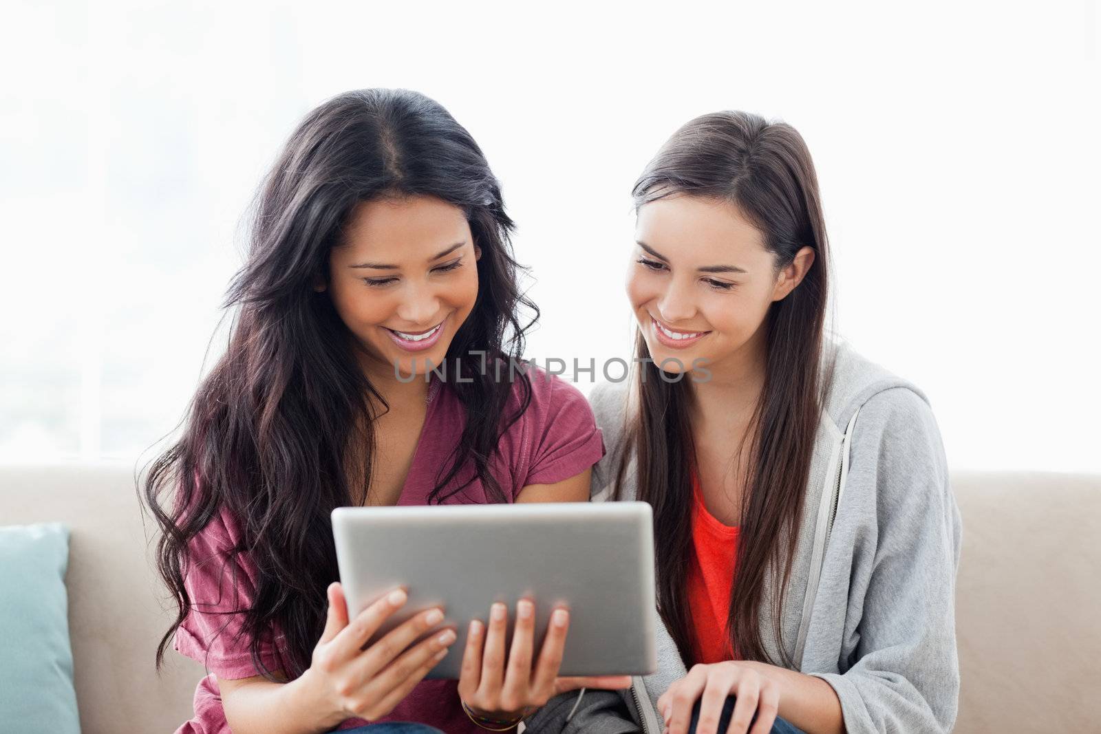 A woman with her friend smiling as they both look at the tablet  by Wavebreakmedia