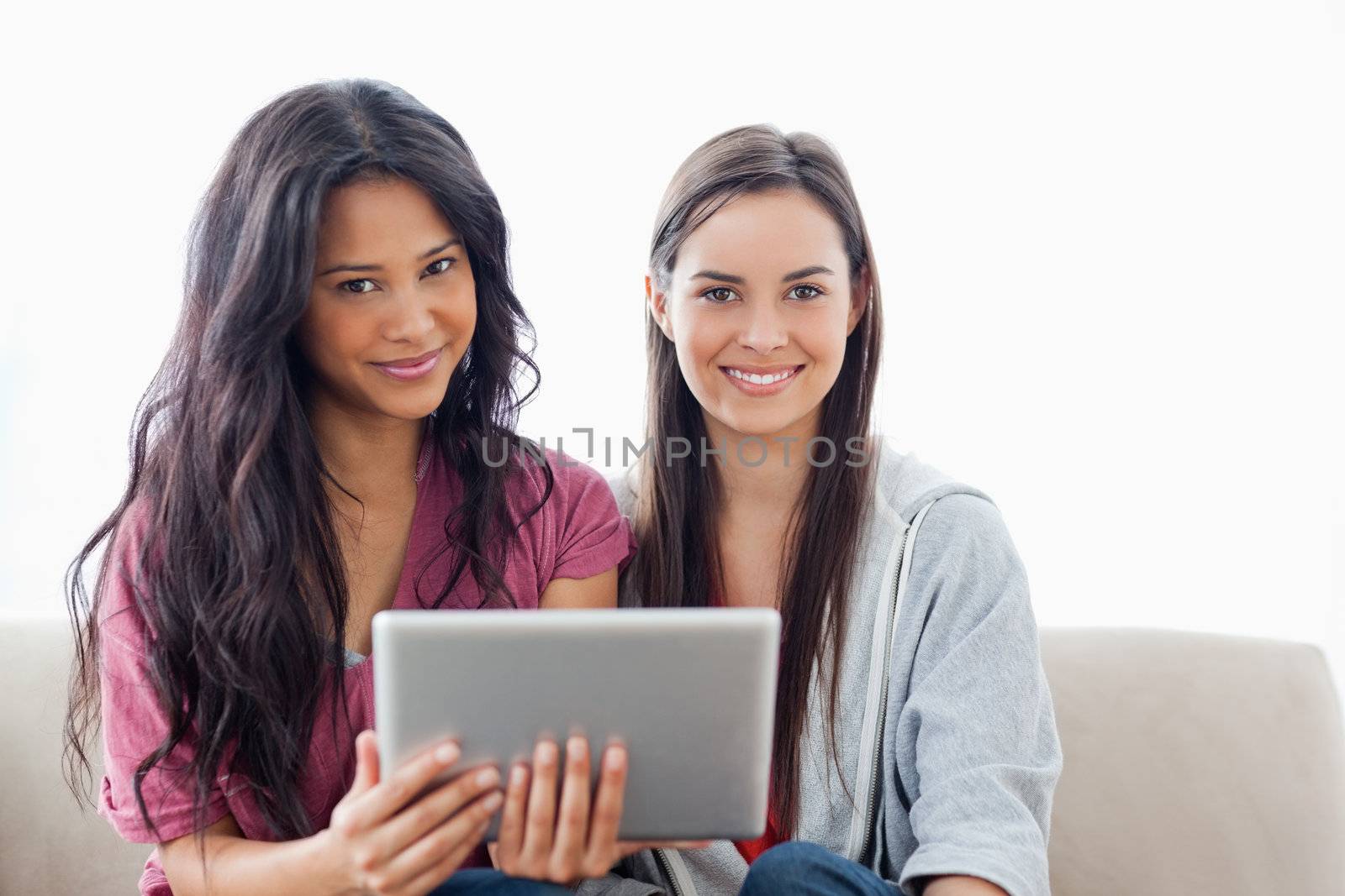 Two ladies with a tablet pc in hand looking at the camera by Wavebreakmedia
