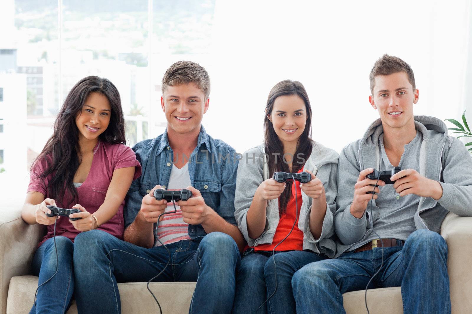 A smiling group of friends sit on the couch with controllers playing a game together 