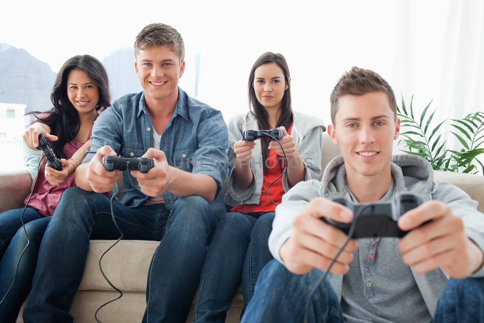 A smiling group of friends playing together on a console while looking into the camera