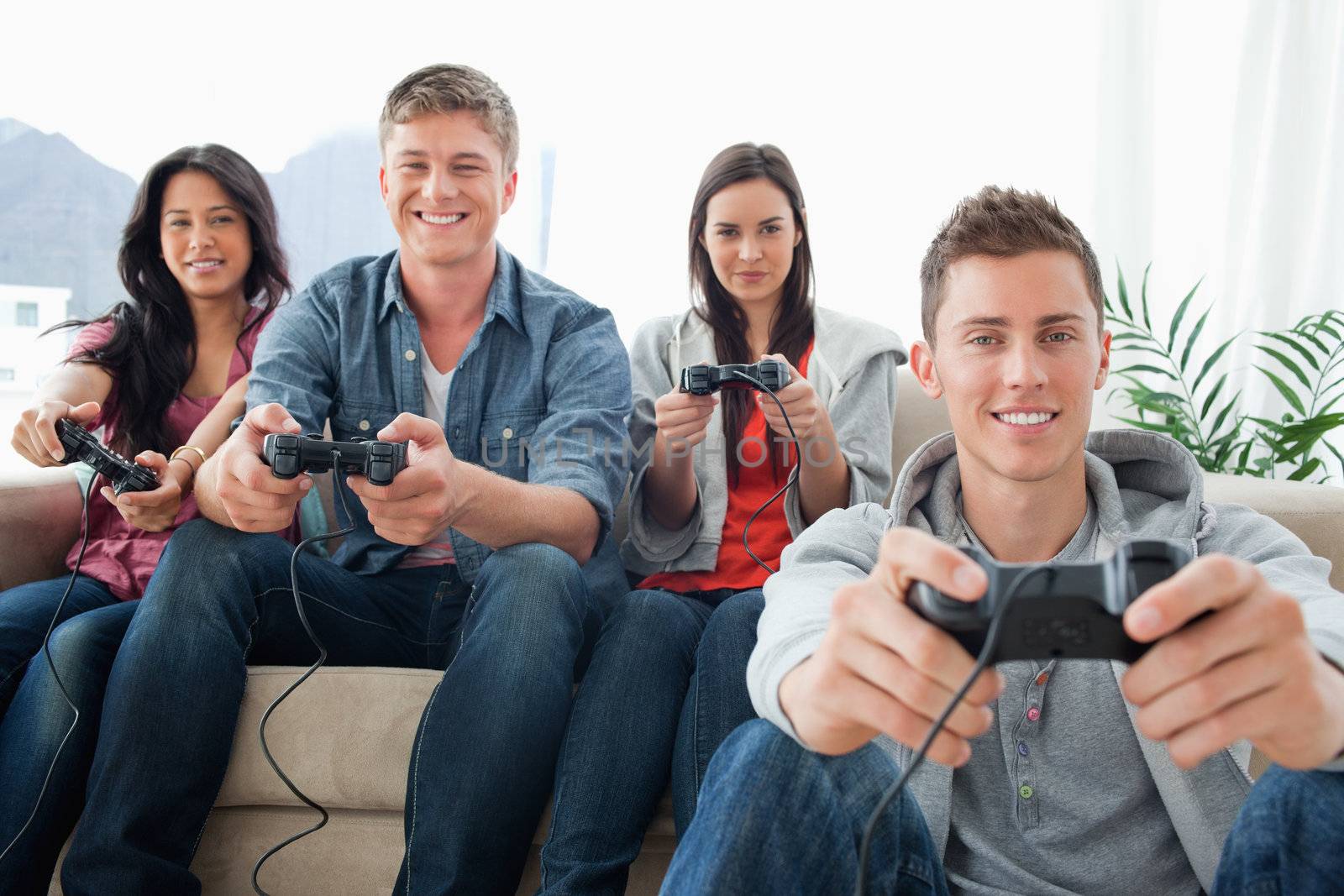 A smiling group of friends playing games together while sitting on the couch as one man sits on the ground as they all look into the camera