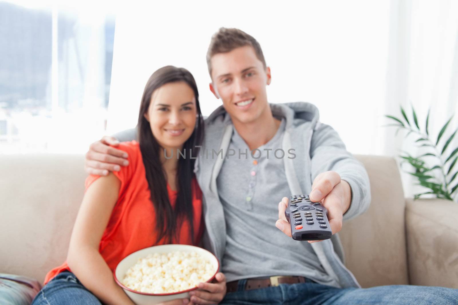 Focus shot on the remote in the man's hand as the couple embrace by Wavebreakmedia