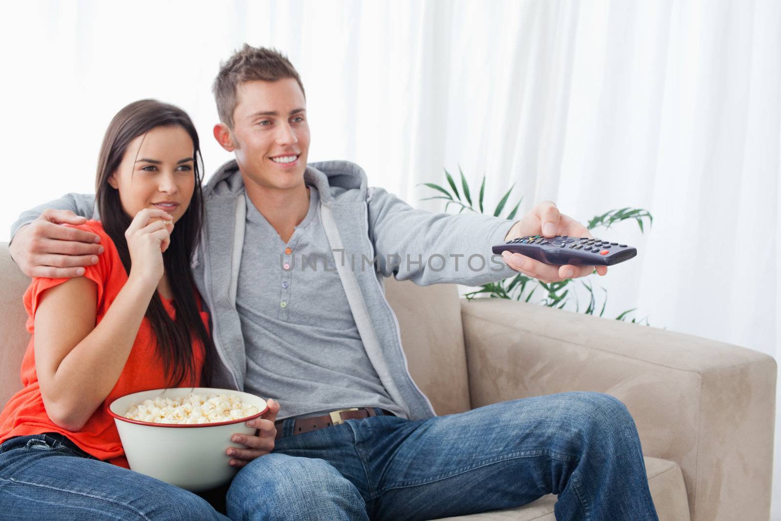 A side view shot of a smiling couple enjoying a tv show while having popcorn