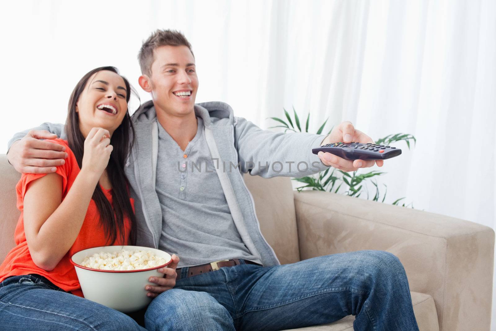 An embracing laughing couple enjoying a tv show as they eat popc by Wavebreakmedia