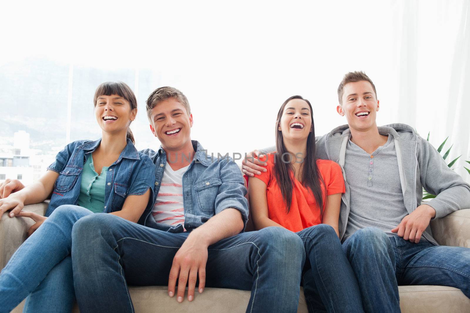 A laughing group of friends look ahead into the camera while on the couch