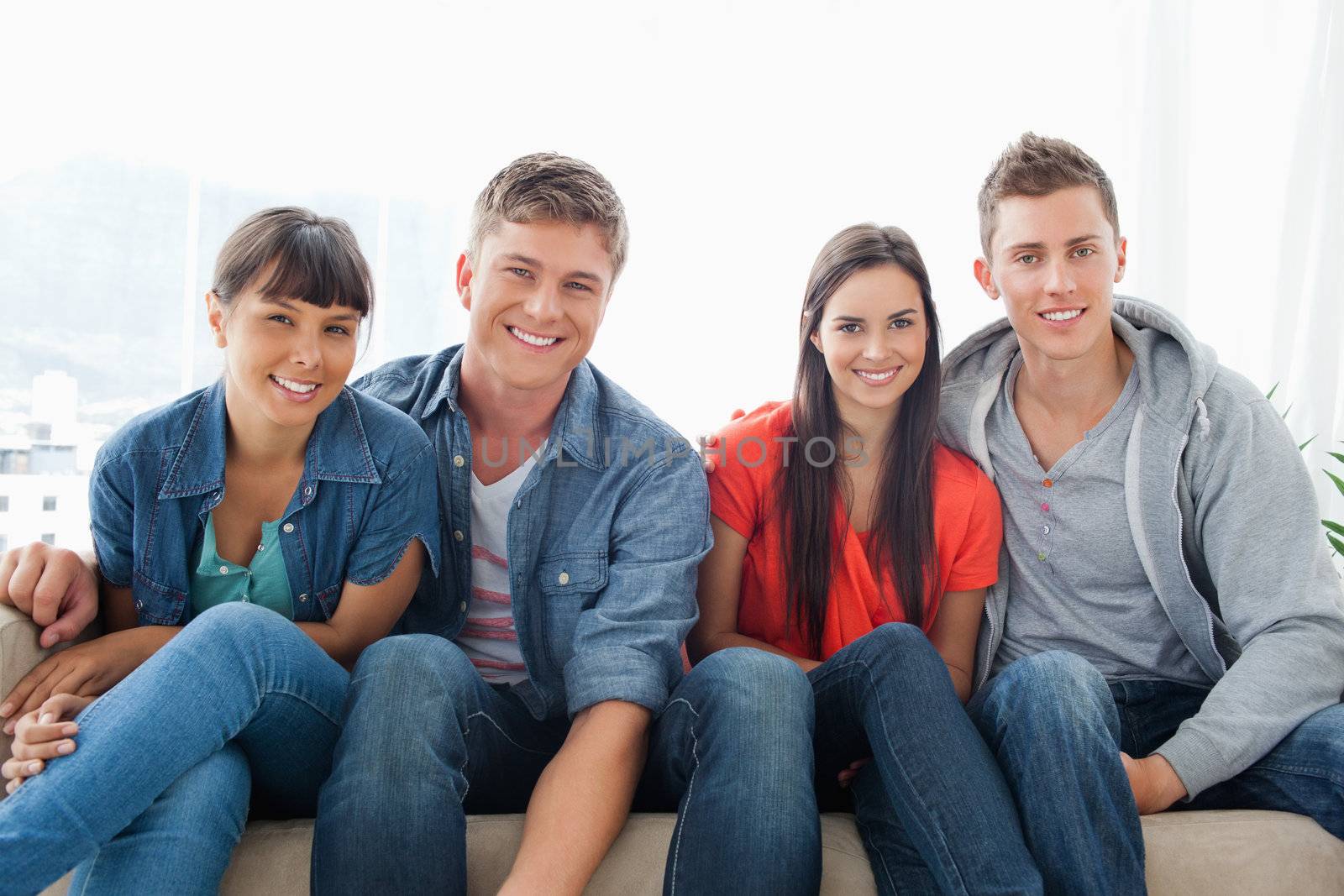 A smiling group leaning forward slightly as they look into the camera while sitting on the couch