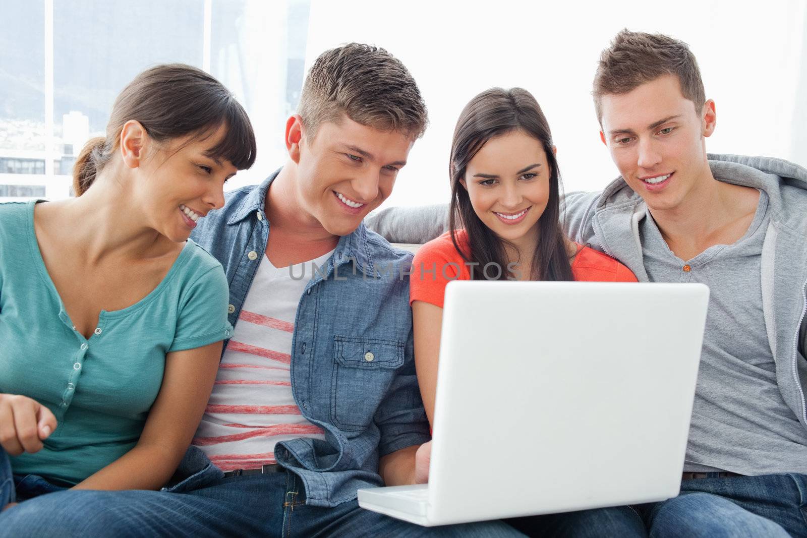 A group of friends sitting on the couch together smiling as they look at a laptop