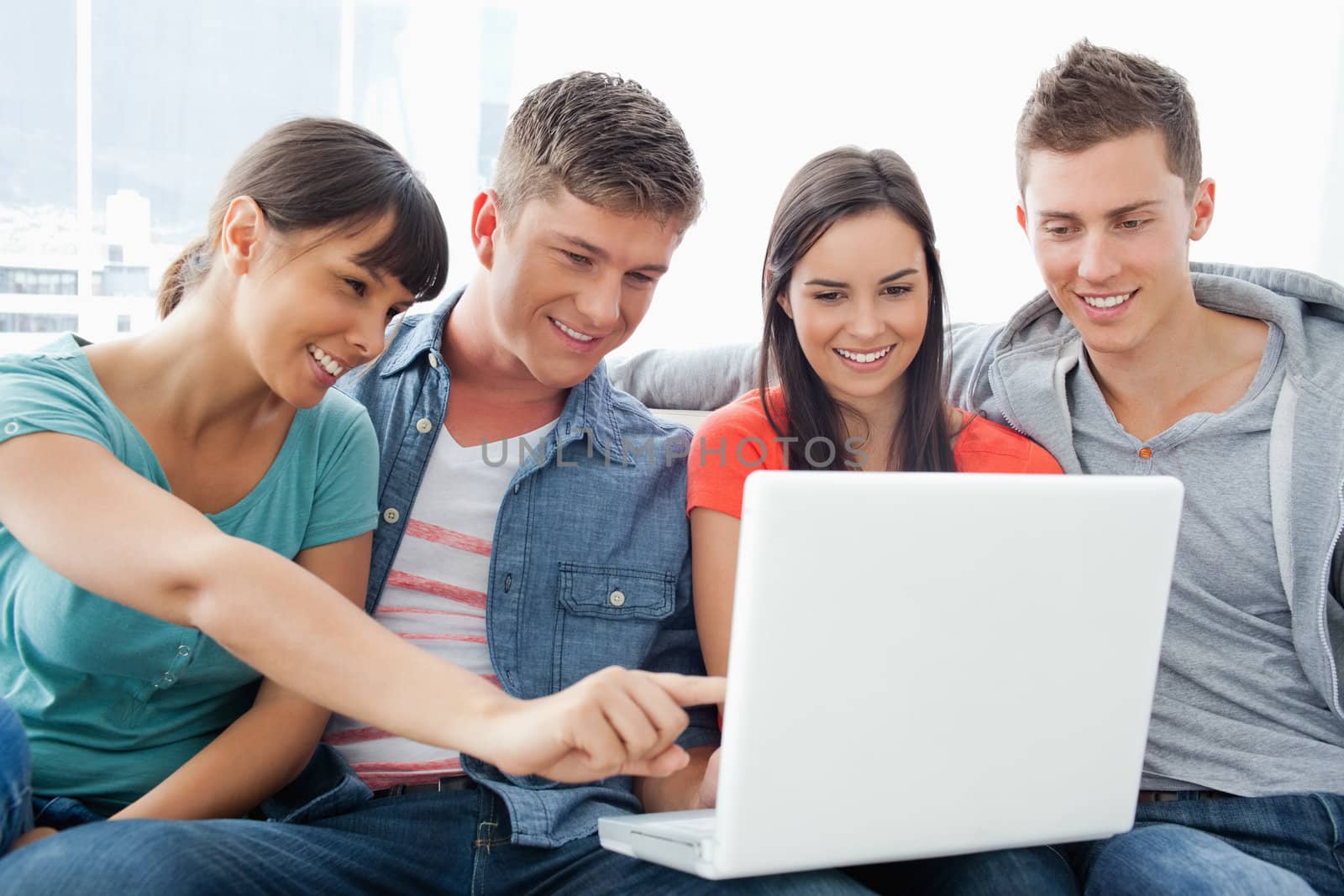 A group of friends smiling as they watch the screen of the laptop with one girl pointing something out 