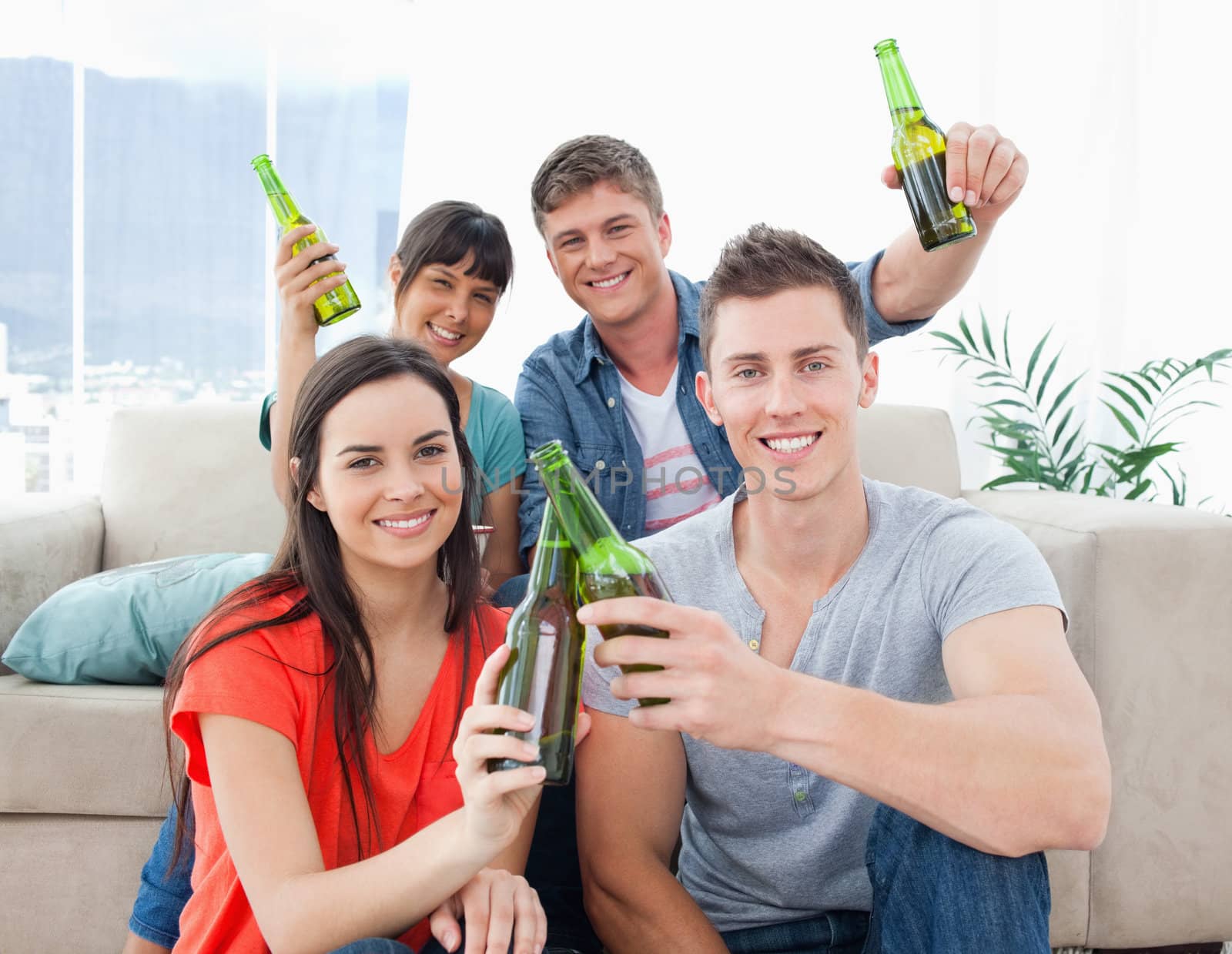 A group of friends indoors celebrating by clinking bottles and toasting 