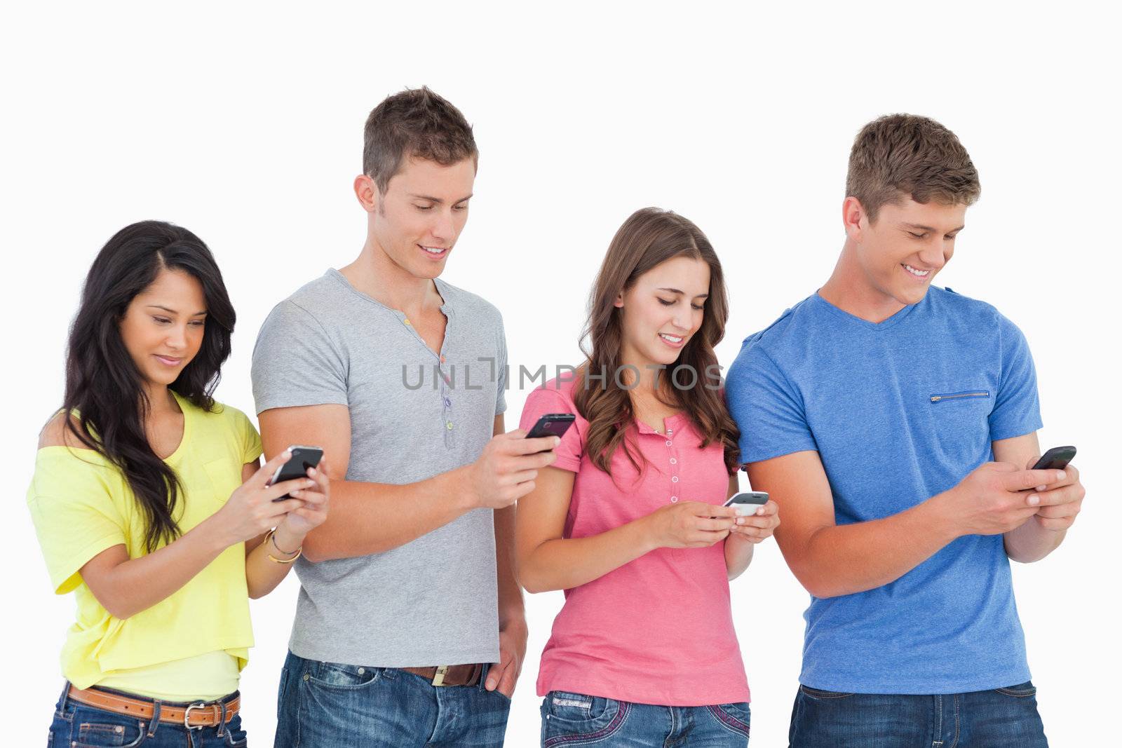 A group of four friends standing slightly to the side as they all send texts on their phones 