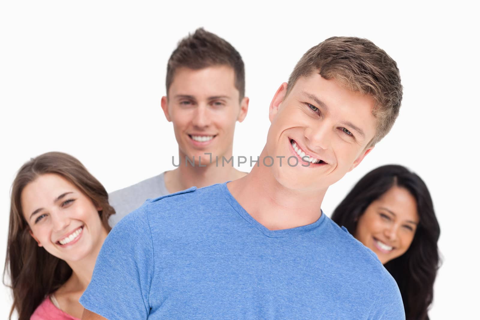 A smiling man with his head tilted as his friends stand behind him doing the same in different directions