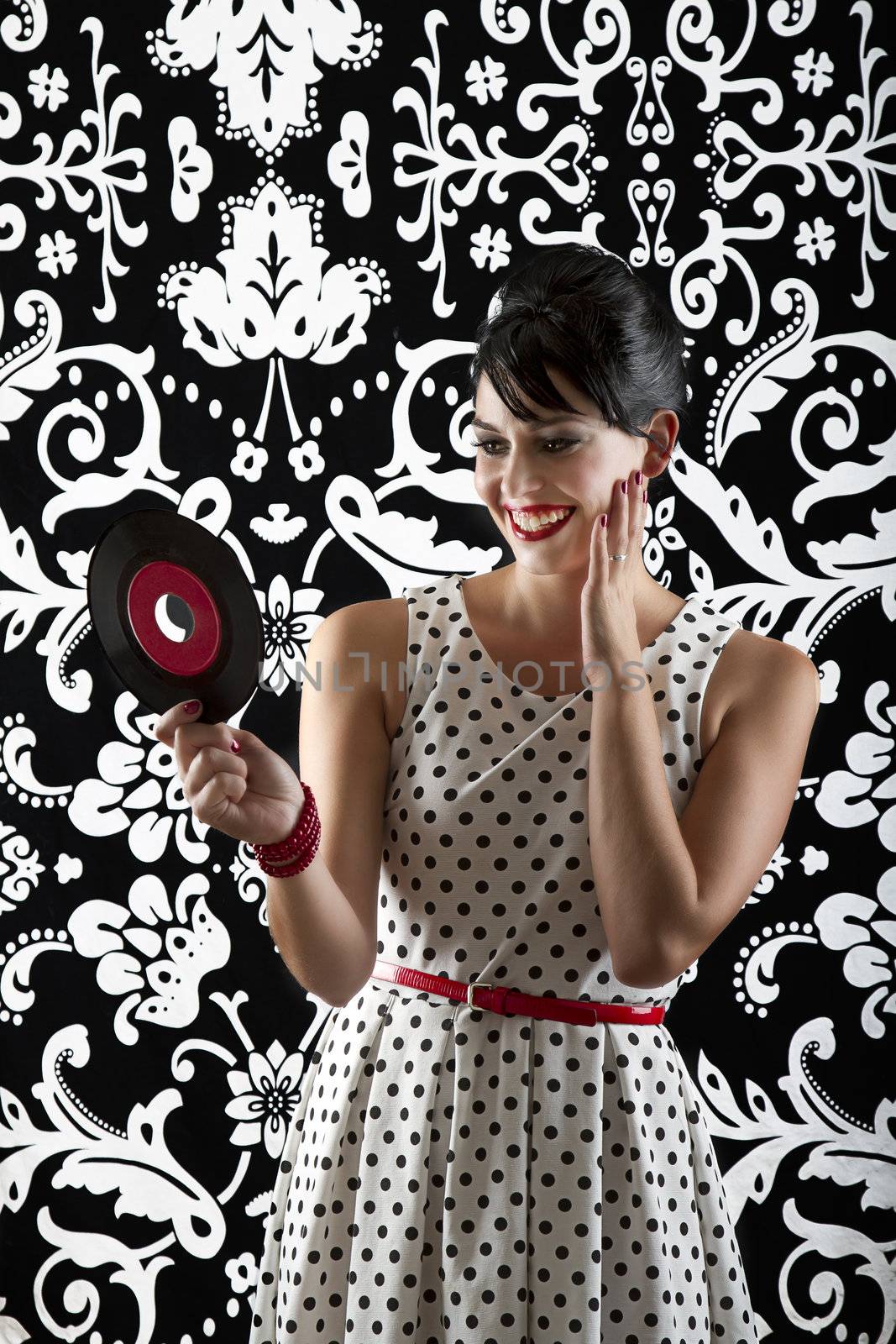 young woman in front of a black and white textured background with 60's inspired style, holding a small record with a red label