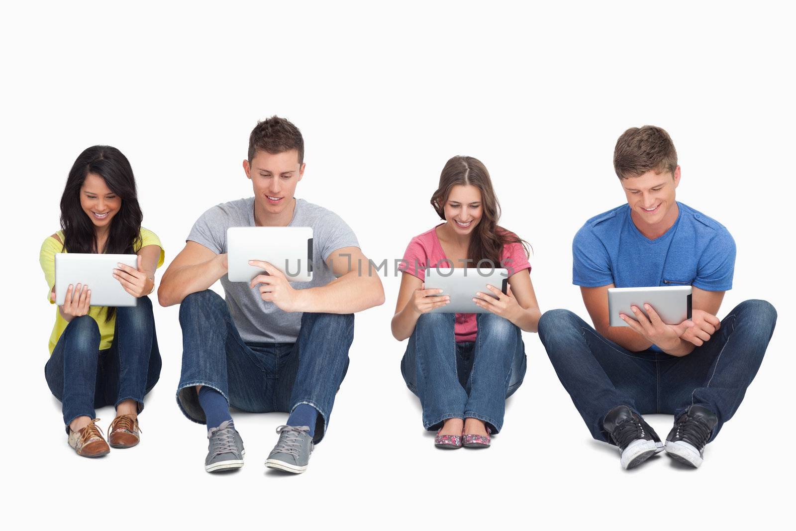 Four smiling friends sitting on the ground beside each other using tablet pc's