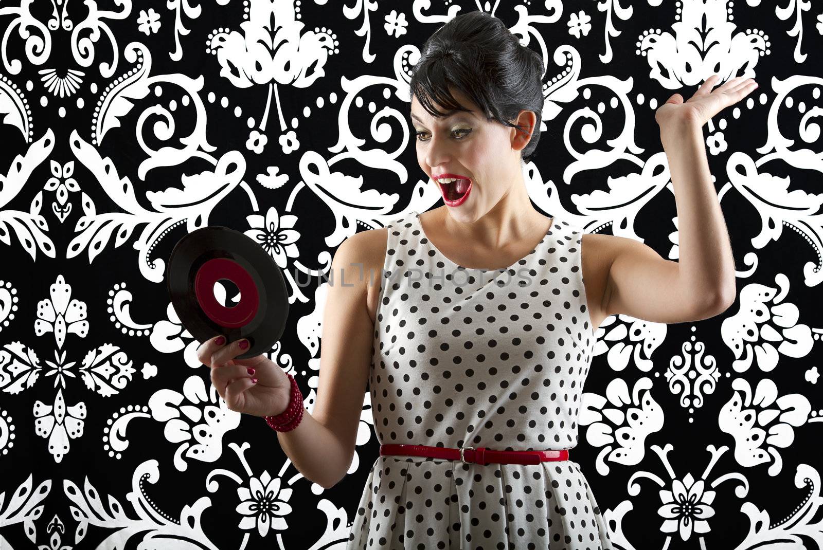 young woman in front of a black and white textured background with 60's inspired style, holding a small record with a red label