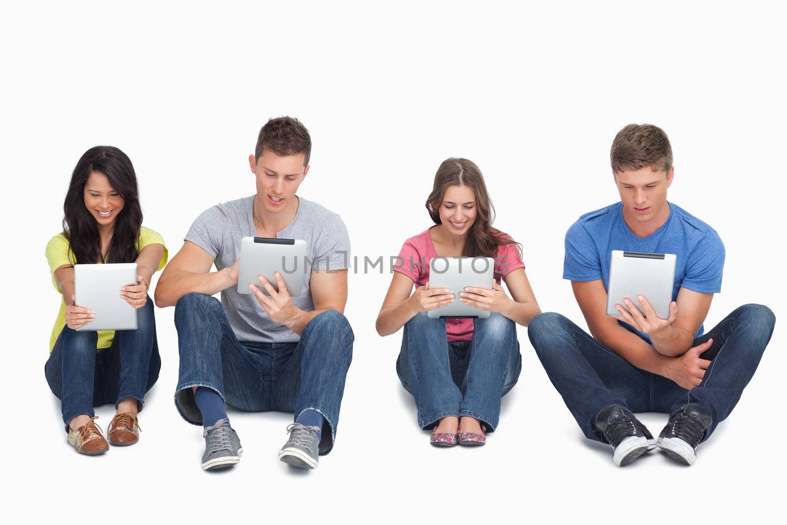 A group of four people sitting beside each other on the ground as they all use their tablet pc's