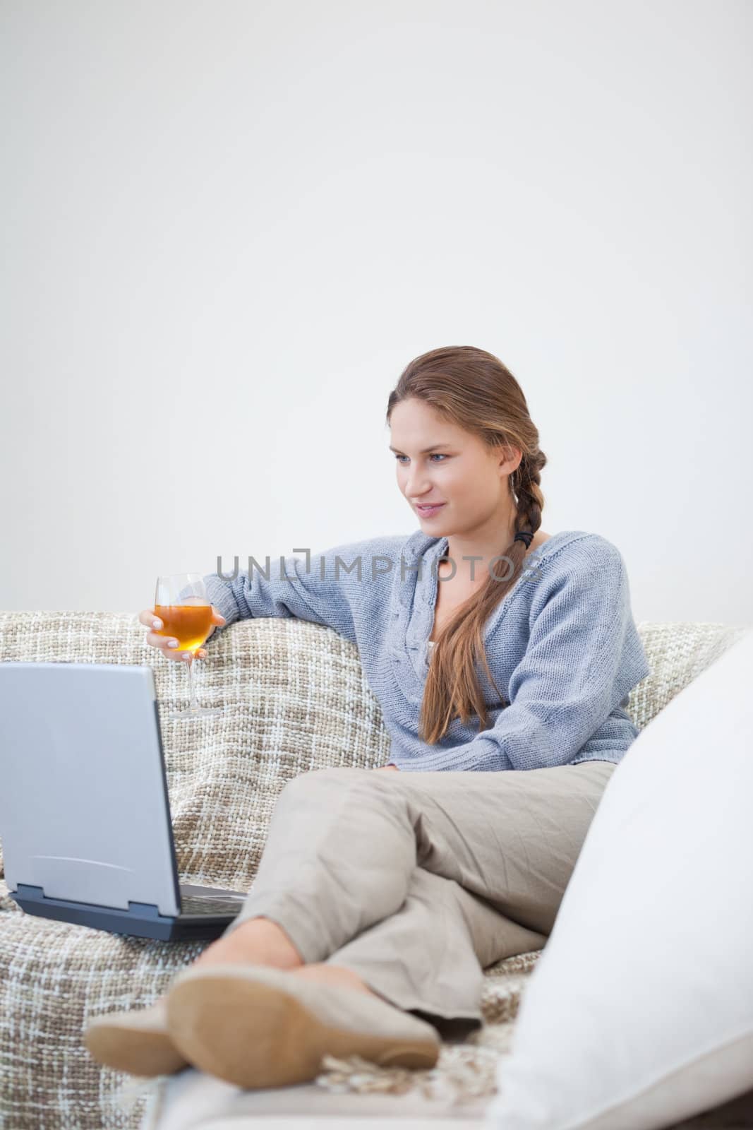 Woman sitting and holding a glass while looking on a laptop indoors