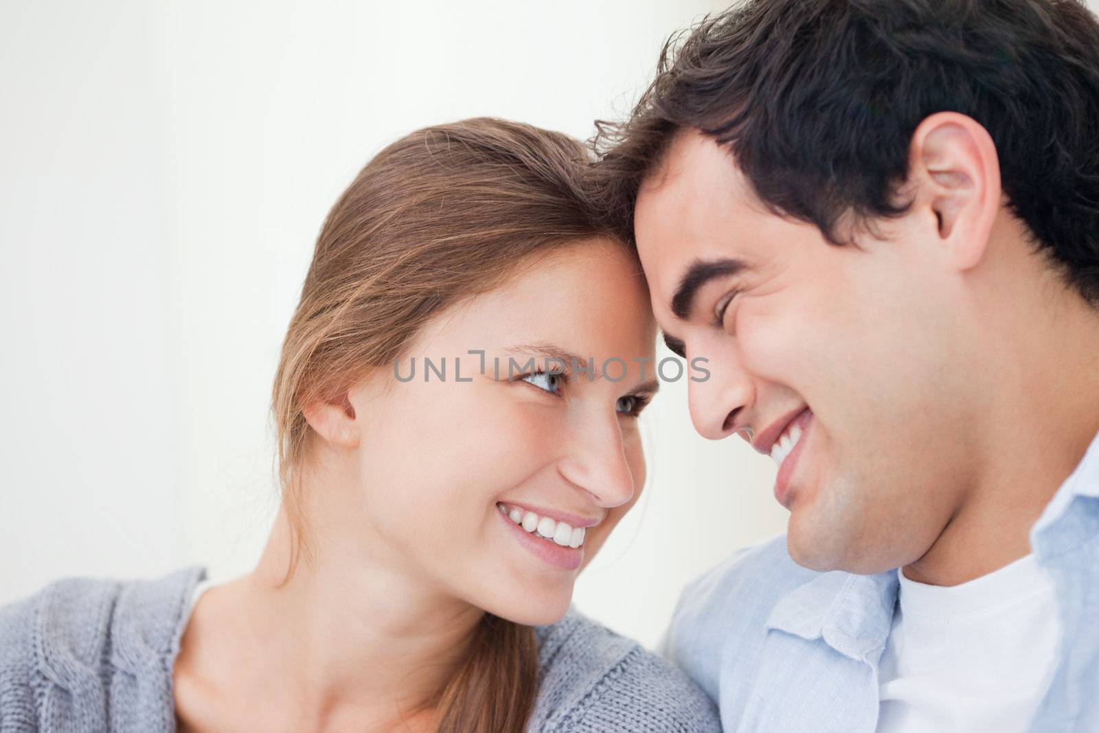 Couple smiling while touching forehead against grey background