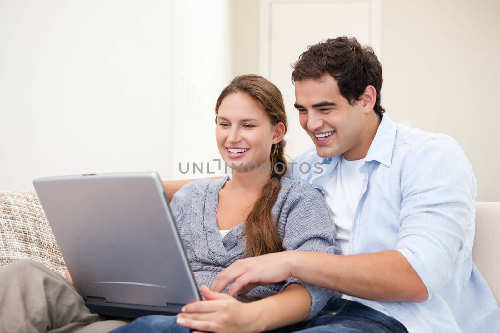 Couple sitting on a sofa while holding a laptop indoors