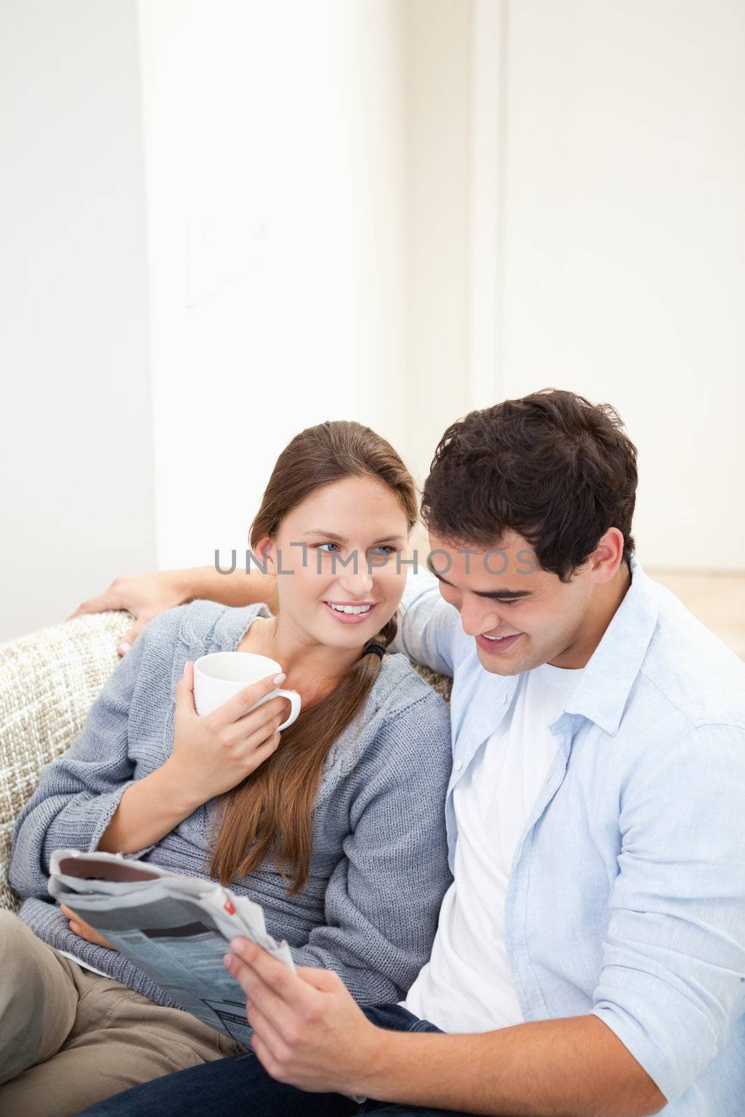 Couple sitting on a sofa while reading a newspaper by Wavebreakmedia