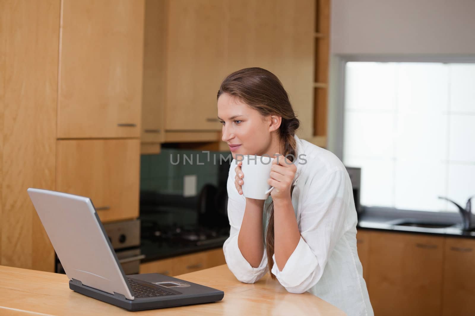 Woman looking at a computer while holding a cup in a kitchen 