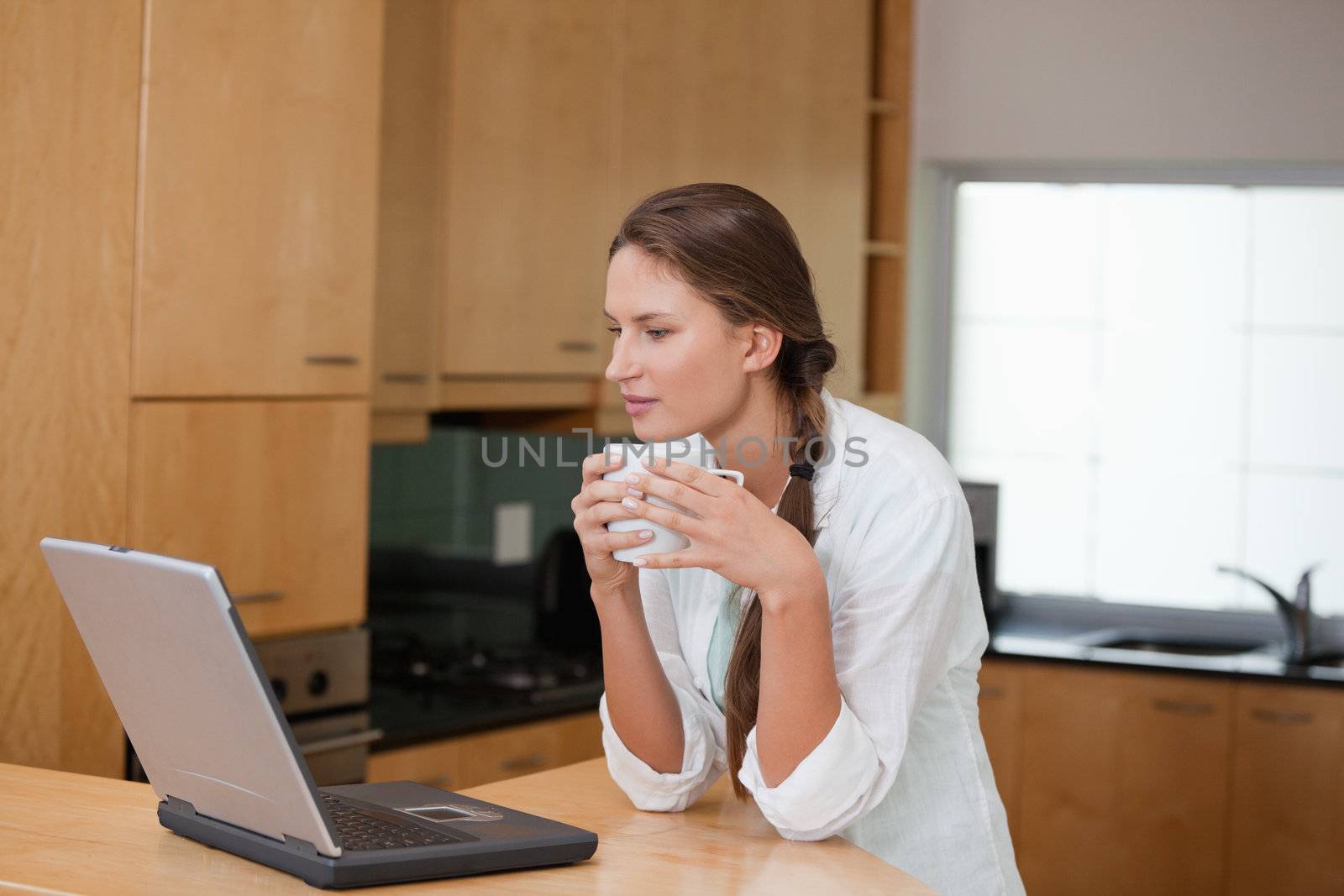 Woman holding a cup while looking at a computer in a kitchen